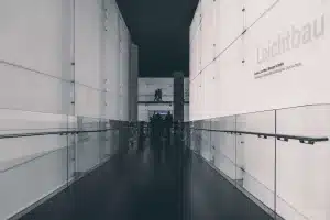 Interno di una galleria d'arte contemporanea con pareti bianche, opere sparse e visitatore solitario