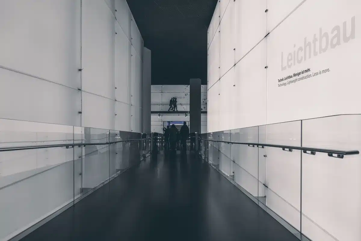 Interno di una galleria d'arte contemporanea con pareti bianche, opere sparse e visitatore solitario