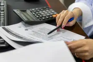 Mani di una persona che tiene documenti finanziari ufficiali su una scrivania con carte sovrapposte