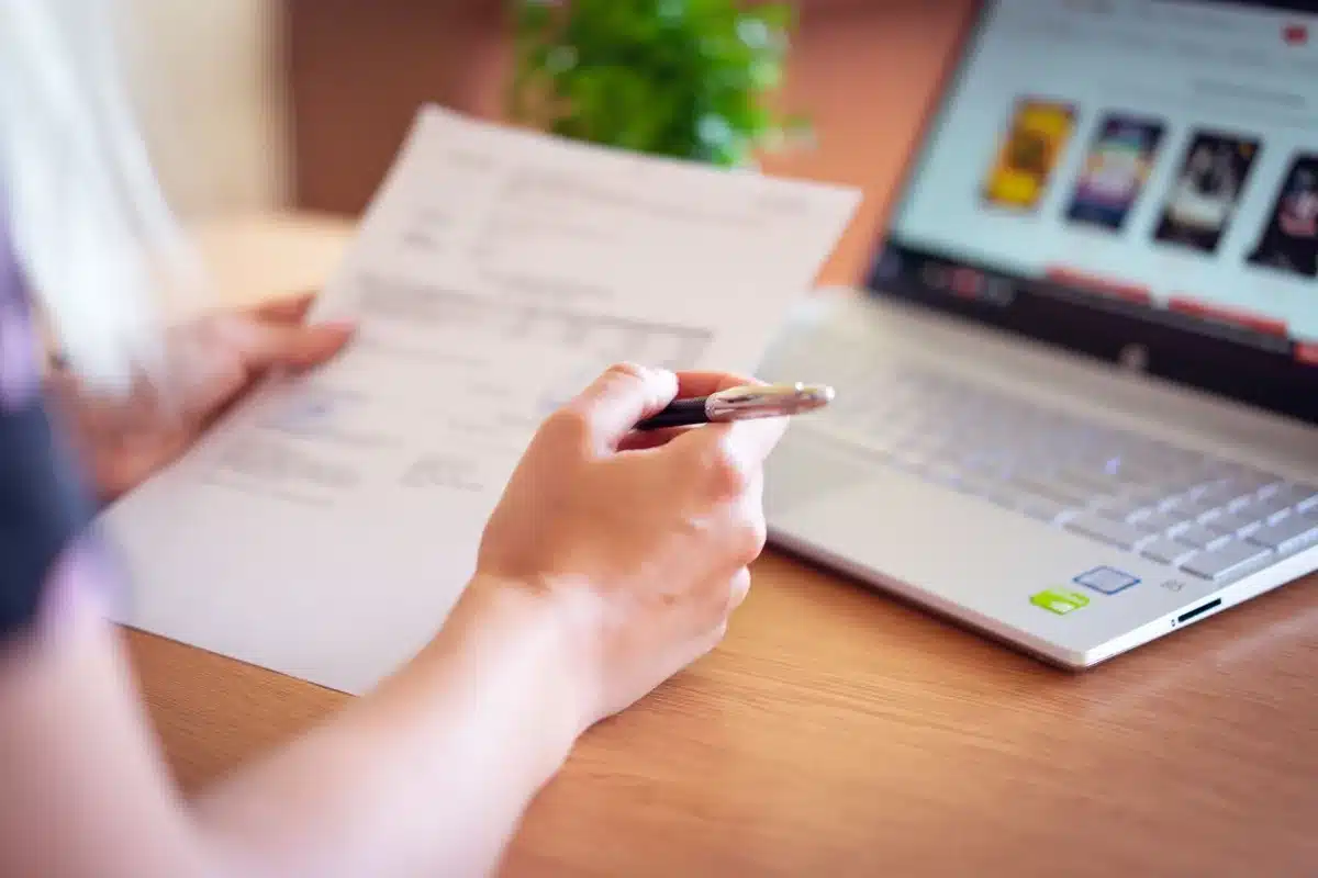 Persona che esamina documenti finanziari su un laptop alla scrivania con carte sparse