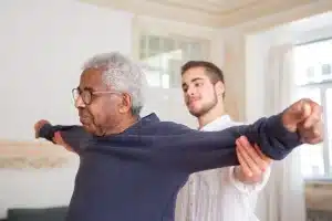 Le mani di un caregiver sostengono il braccio di una persona anziana in un ambiente domestico