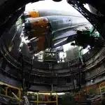Hangar con motori di razzo e silhouette anonime, evocando l'industria spaziale